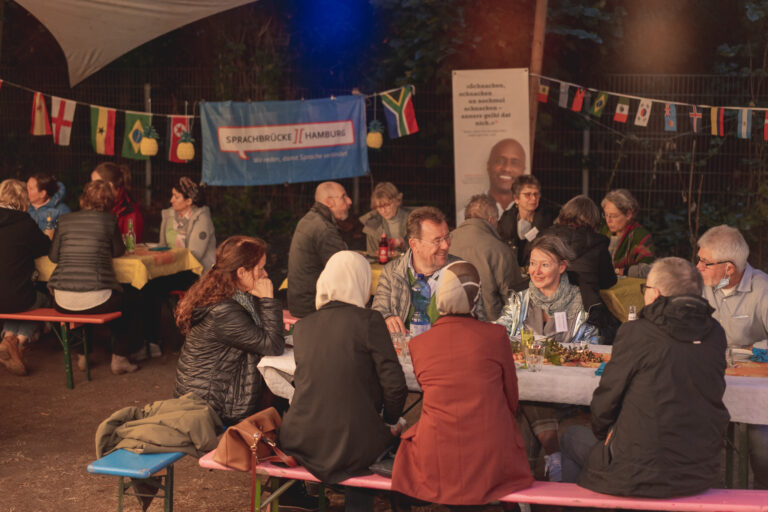 Mehrere Personen sitzen zusammen auf einer Bierbank, wahrscheinlich bei einem gemeinsamen Fest