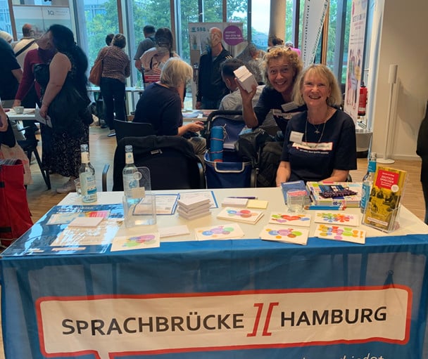 Sprachbrücke-Hamburg e.V. war mit einem Stand auf der „Integrationsmesse Bergedorf“ vertreten. Auf dem Bild sind zwei gut gestimmte Frauen zu sehen.