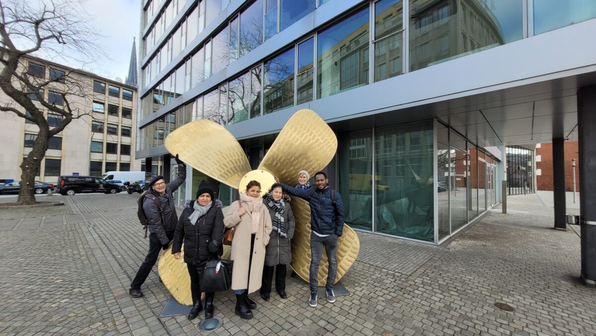Eine Personengruppe aus Frauen und Männern steht vor einer großen Schiffsschraube in der Hamburger Innenstadt