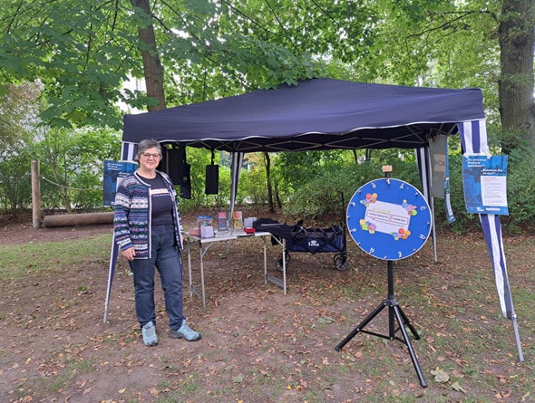 Der Stand von Sprachbrücke-Hamburg e.V. bei der „Lokstedt-Rallye 2024“. Im Hintergrund Bäume, vor dem Stand das Glücksrad von Sprachbrücke-Hamburg e.V.