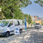 Weißer Sprinter seitlich zu sehen mit offener Schiebetür. Innen eine Gesprächsleiterin von Sprachbrücke-Hamburg e. V. sitzend. Davor ein Plakataufsteller und ein Werbesegel. Im Hintergrund ein Gebäude